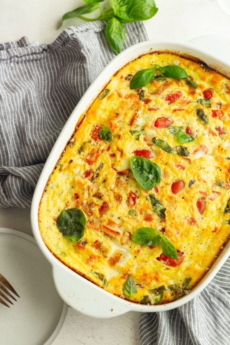 a white 9x13 baking dish full of baked fluffy cottage cheese egg bake loaded with basil and cherry tomatoes