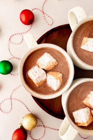 a photo taken over the top of three mugs of creamy hot cocoa each with 3 large marshmallows floating in them
