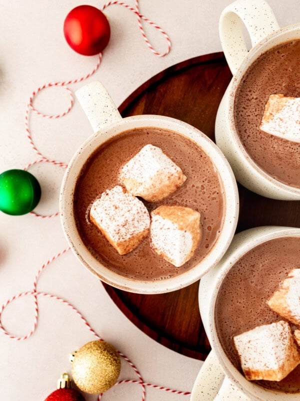 a photo taken over the top of three mugs of creamy hot cocoa each with 3 large marshmallows floating in them