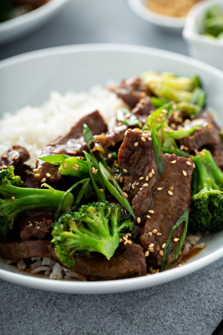 A close up of broccoli beef on a plate next to white rice.