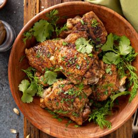 A bowl filled with five Jerusalem Herbed Chicken Thighs topped with cilantro leaves and dill leaves