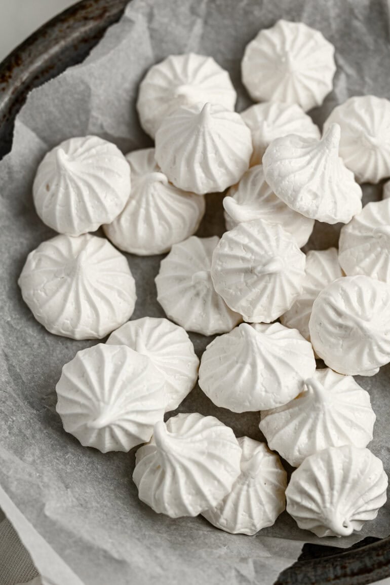 several white piped small meringue cookies in a bowl lined with white parchment paper