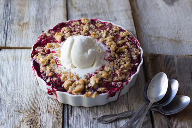 a photo of a marionberry crisp in a shallow tart dish with a scoop of vanilla ice cream melting on top