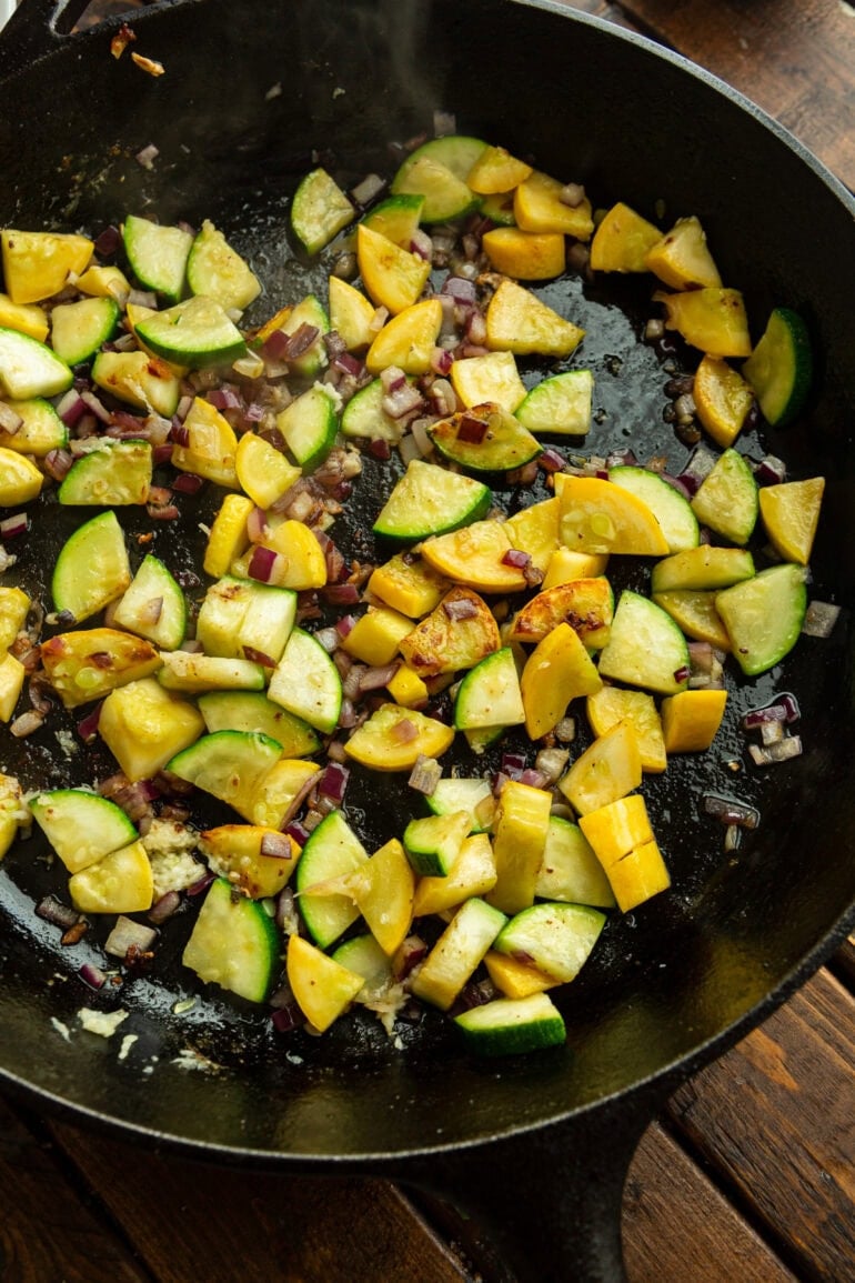 chunks of zucchini and yellow squash being sauteed in a cast iron skillet