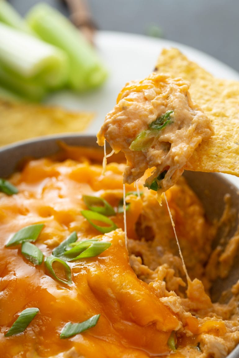 Buffalo chicken dip. There is a tortilla chip that has been dipped in. You can see shredded chicken in a creamy orange buffalo sauce topped with melted cheese and chopped green onions.