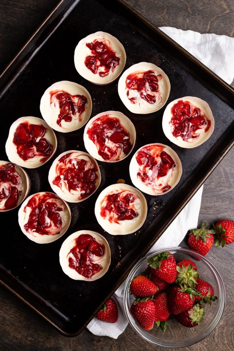 Individual cups of cheesecake batter with a bright strawberry swirl.