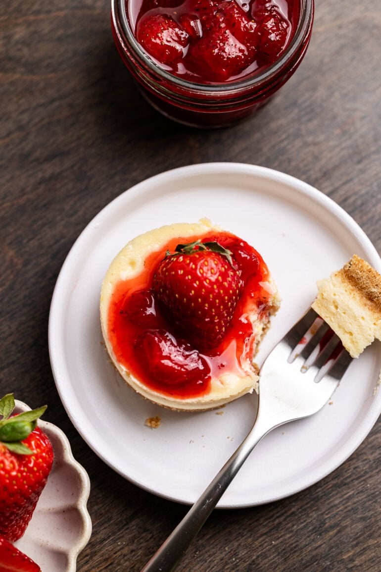 A fork is taking a single bite out of a personal sized cheesecake with berry topping