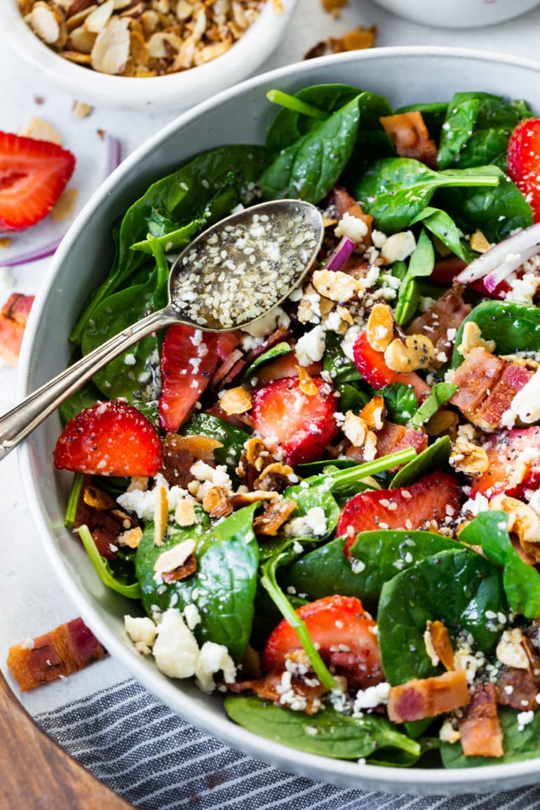 a photo of a strawberry feta spinach salad with a silver spoon sitting on top full of homemade poppy seed dressing.