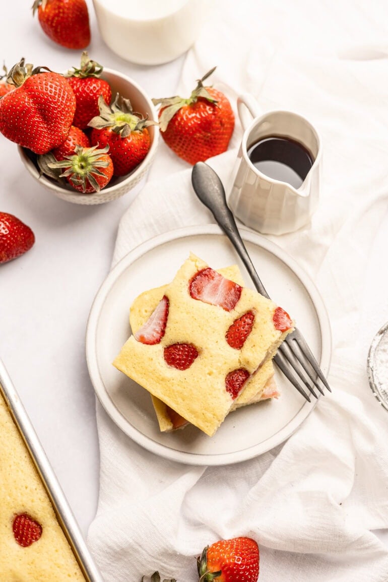 two sheet pan pancakes stacked on each other sitting on a white plate with a fork sitting next to them