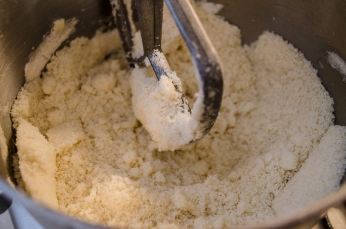 A stand mixer bowl full of a sandy mixture of softened butter and dry ingredients. The paddle attachment has blended them together, creating the perfect base for a light and fluffy cake.