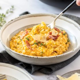 A grey bowl on a dark grey napkin. It's filled with orange coloured risotto