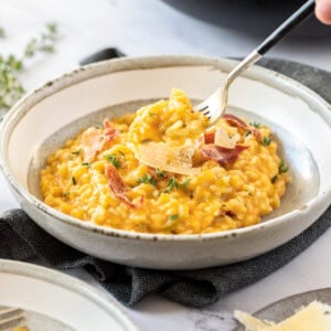 A grey bowl on a dark grey napkin. It's filled with orange coloured risotto