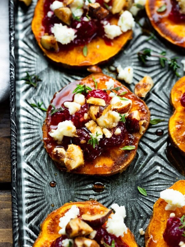a photo of a roasted sweet potato round topped with cranberry sauce, feta cheese, and hazelnuts.