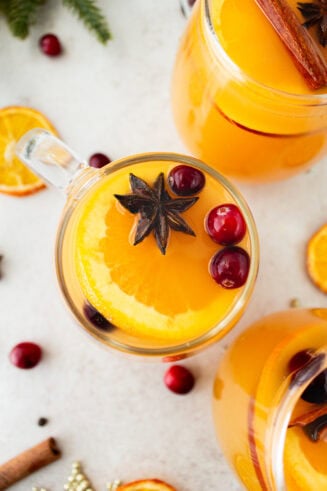 a photo taken over the top of a glass mug full of bright orange homemade wassail topped with floating whole cranberries and star anise