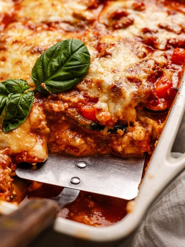 a metal spatula scooping out a serving of cheesy, saucy zucchini lasagna