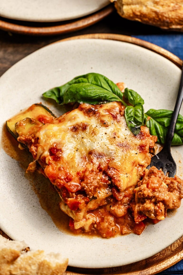 Our best zucchini fancy noodles ever! ohsweetbasil.com A plate with a layered zucchini noodles, cheese and meat sauce and basil garnish. A fork is digging slices of lasagna.