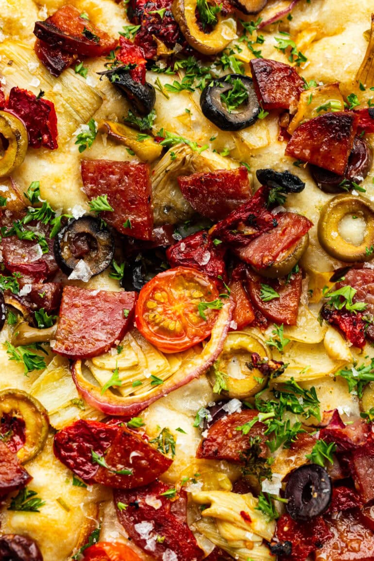 baked loaf of focaccia bread topped with chopped meats, cherry tomatoes, green and black olives and red onions