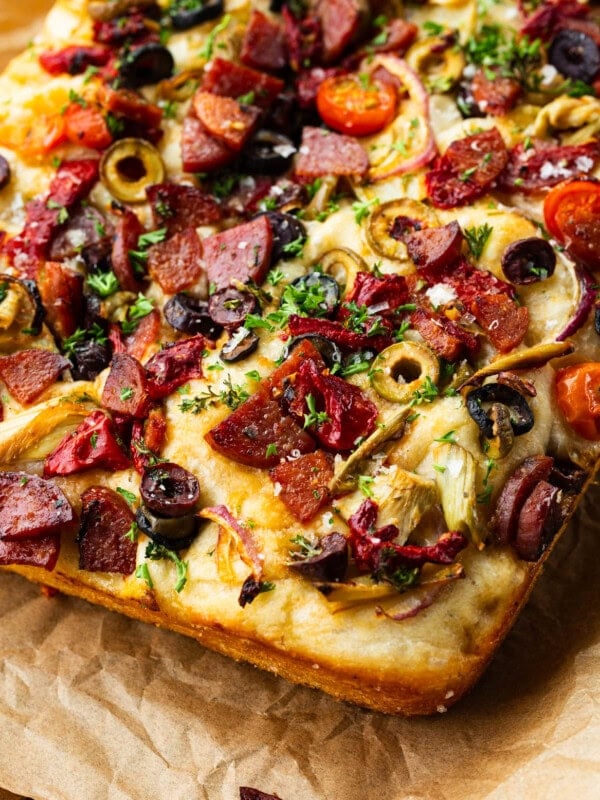 a baked loaf of antipasto focaccia bread topped with sliced green olives, chopped meats, sundried tomatoes and herbs