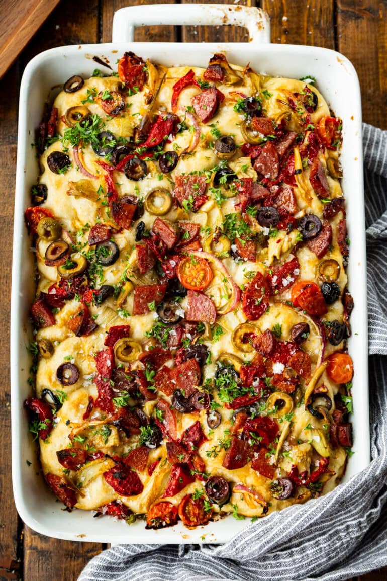 a white casserole dish full of baked italian focaccia bread topped with antipasto