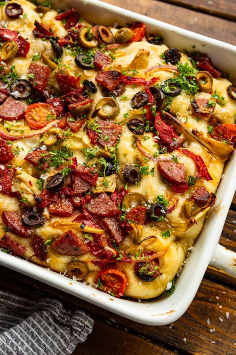 golden baked focaccia bread topped with chopped deli meats, olives, tomatoes, red onion, and artichoke hearts