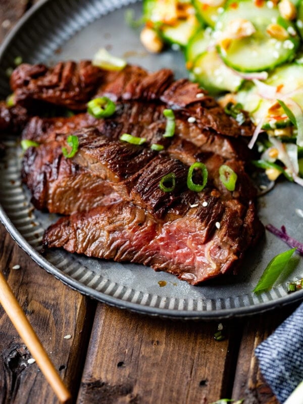 a photo of thin slices of asian marinated flank steaks stopped with chopped scallions with a side of cucumber salad.