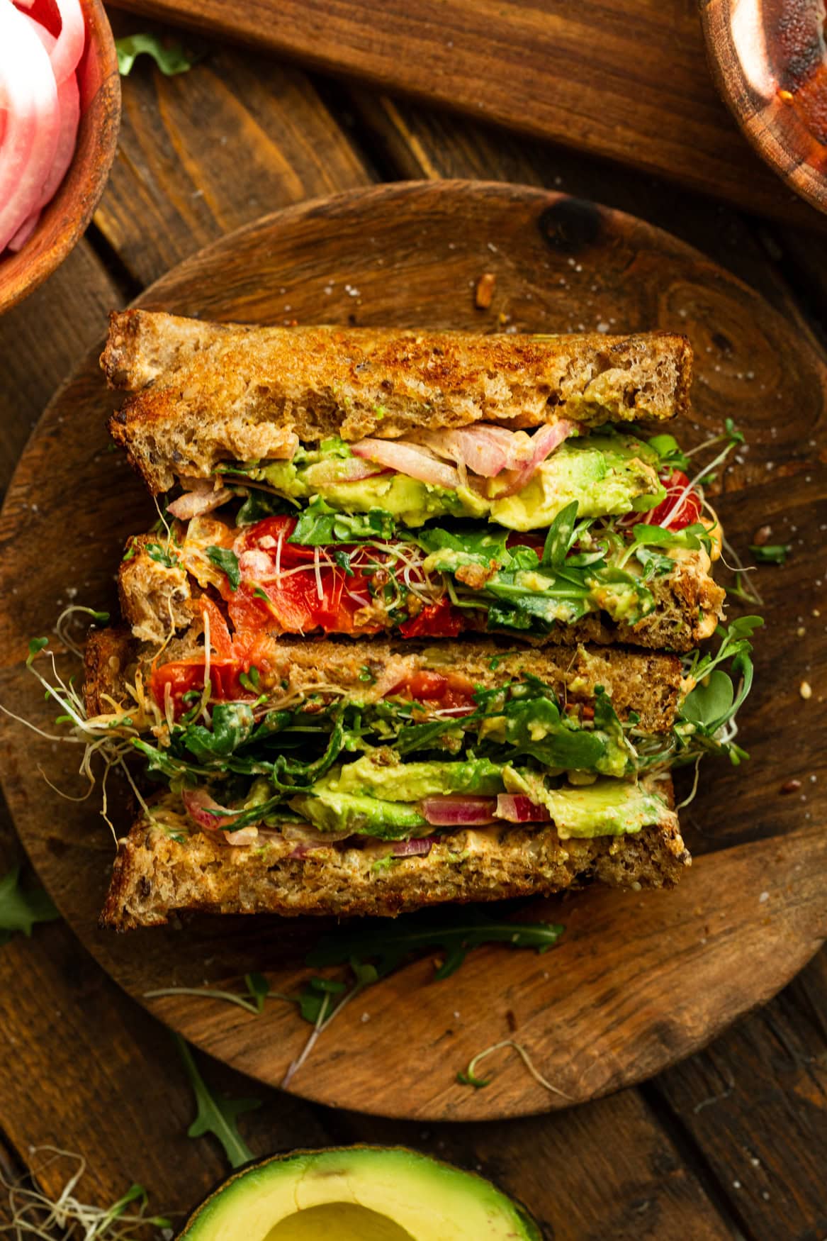 a photo of an avocado sandwich that has been cut in half and then set up on their side so you can see the layers inside the sandwich