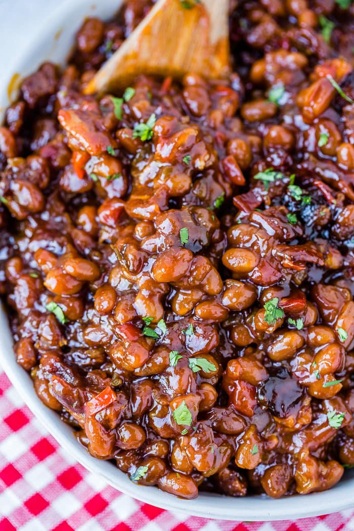 A white bowl full of saucy baked beans with chopped cilantro sitting on a red checkered napkin