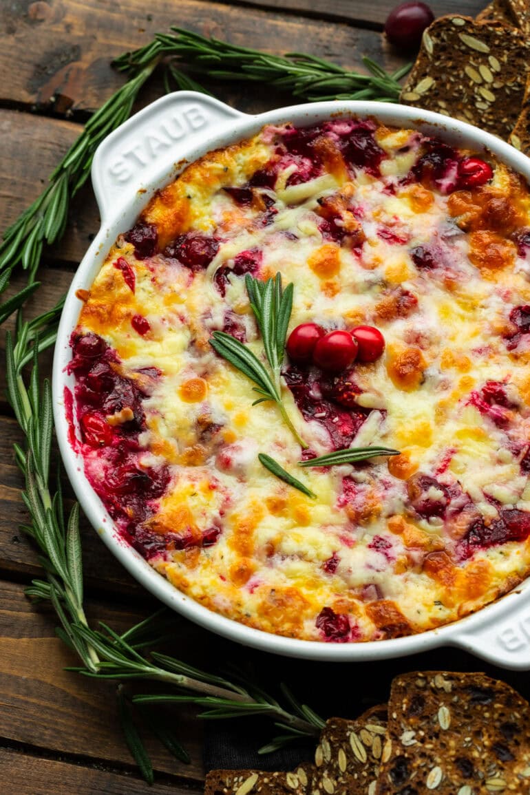 Dip Cheesy Cranberry Cream Cheese into a round cast iron baking pan and top with fresh rosemary and whole cranberries