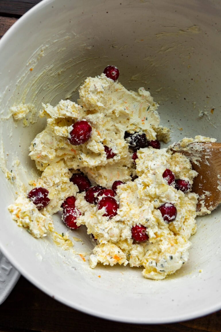 Photo of cream cheese, whole cranberries and grated cheese stirred together in a white bowl with a wooden spoon