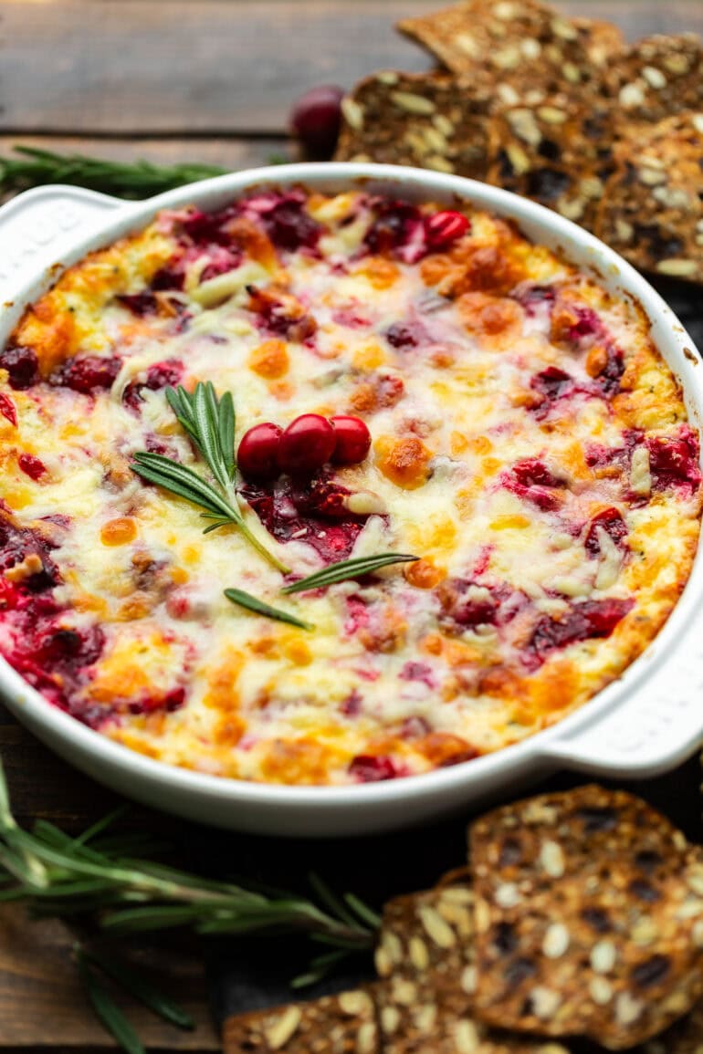 A round cast iron baking pan filled with melted cranberry cream cheese sauce and topped with a sprig of fresh rosemary and a few whole cranberries