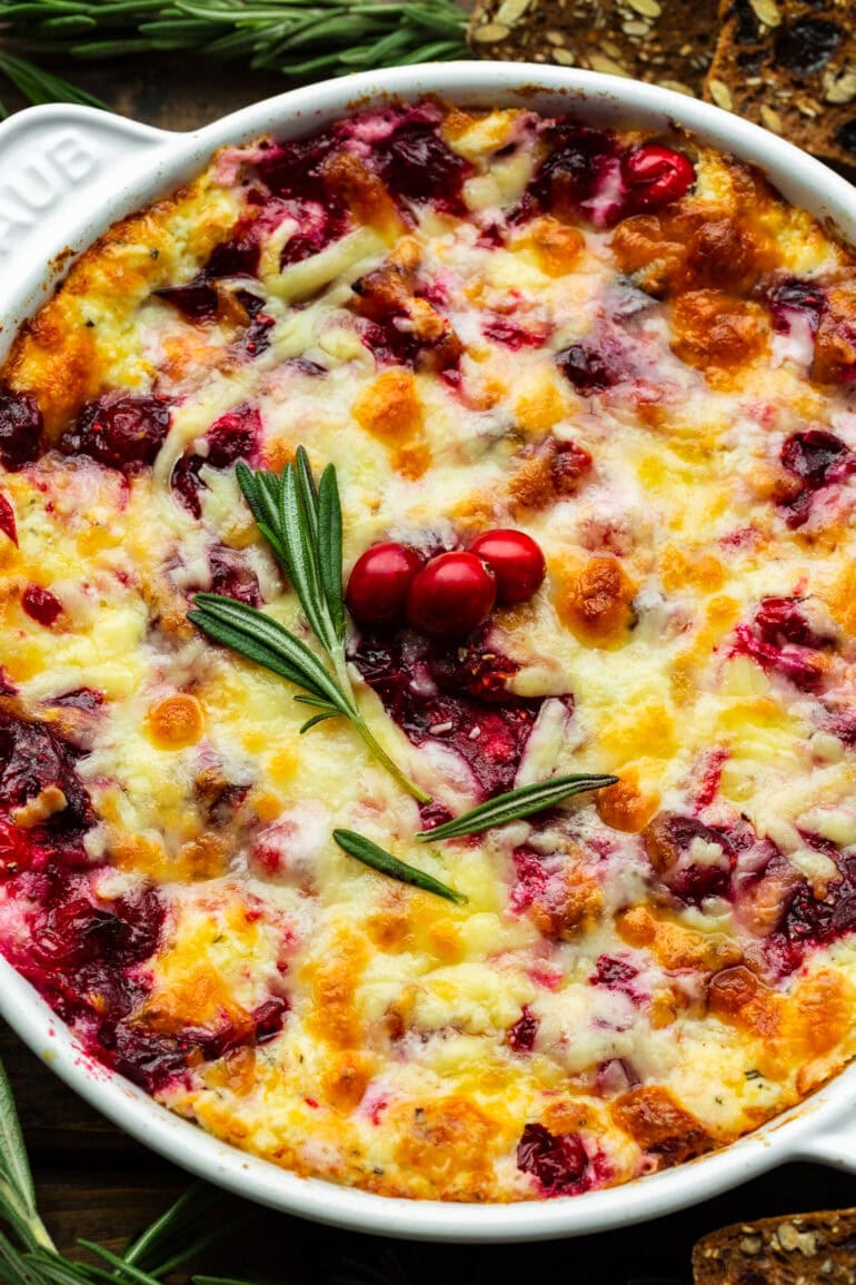Melted Cheesy Cranberry Cream Cheese Dip in a round baking dish topped with fresh rosemary and some whole cranberries
