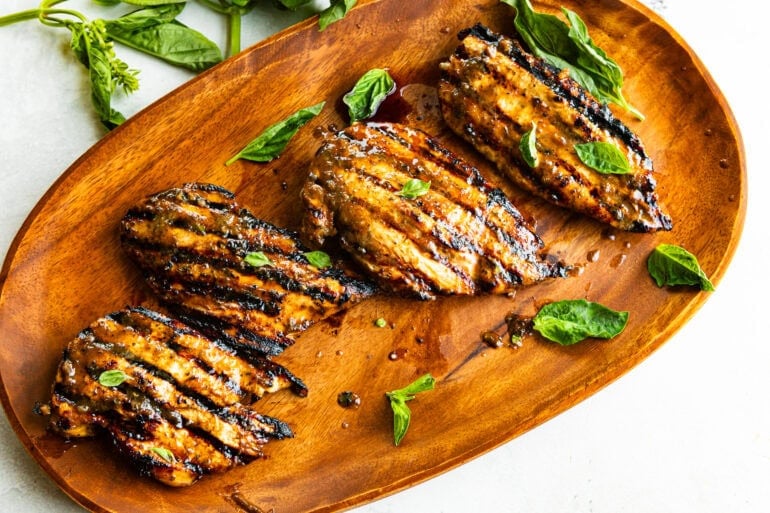4 charred grilled breasts sit on a wooden cutting board. The chicken has a vinegar touch.