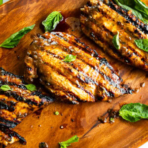 several grilled chicken breasts with basil leaves scattered about it
