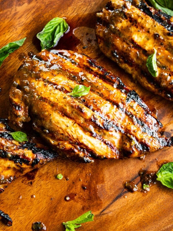 several grilled chicken breasts with basil leaves scattered about it