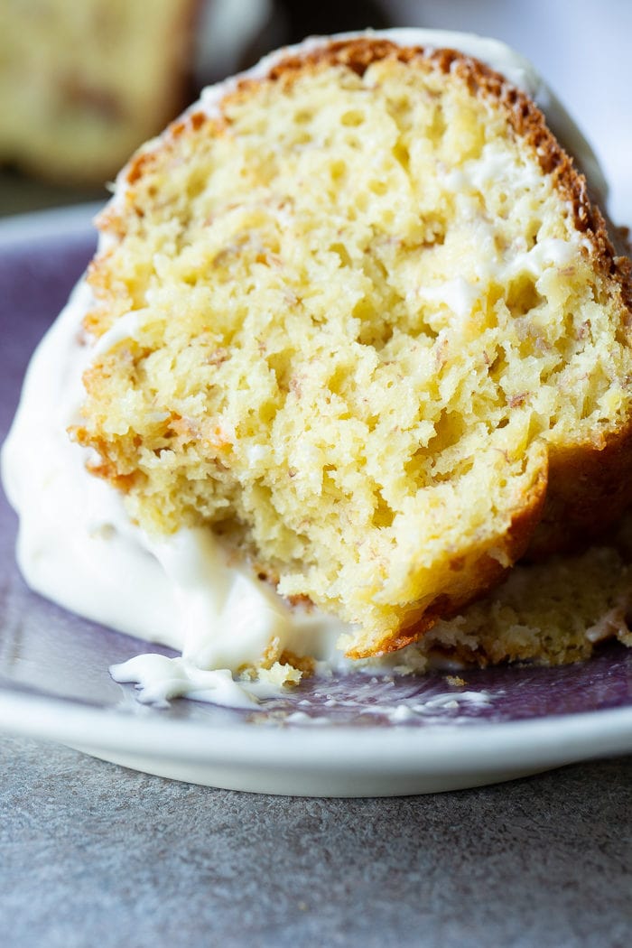 A slice of banana bundt cake with white creamy frosting on a blue plate.