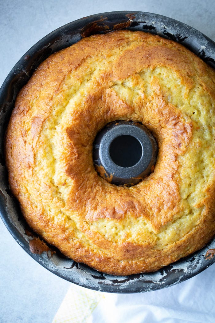 A dark bundt pan with a beautiful, bright yellow banana pudding bundt cake