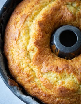 A dark bundt pan with a beautiful, bright yellow banana pudding bundt cake