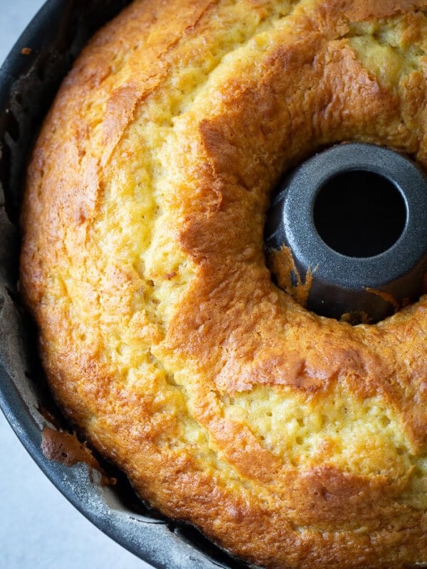 A dark bundt pan with a beautiful, bright yellow banana pudding bundt cake