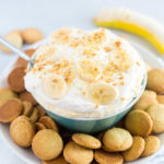 a platter with nilla wafers and a bowl of banana cream pie dip with crushed cookies and sliced bananas on top