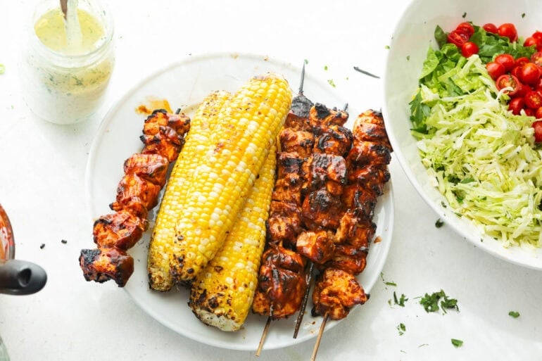 a stack of bbq grilled chicken skewers and two ears of corn that have been grilled