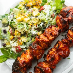 two saucy bbq chicken kabobs with creamy ranch salad on the side on a white dinner plate