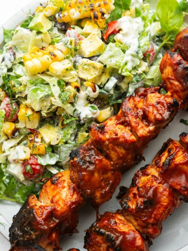 two saucy bbq chicken kabobs with creamy ranch salad on the side on a white dinner plate