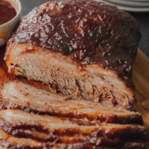 A partially sliced BBQ brisket with a glaze of BBQ sauce on top.