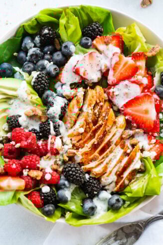 a photo of a berry avocado salad with chicken and candied pecan topped with a creamy poppyseed dressing