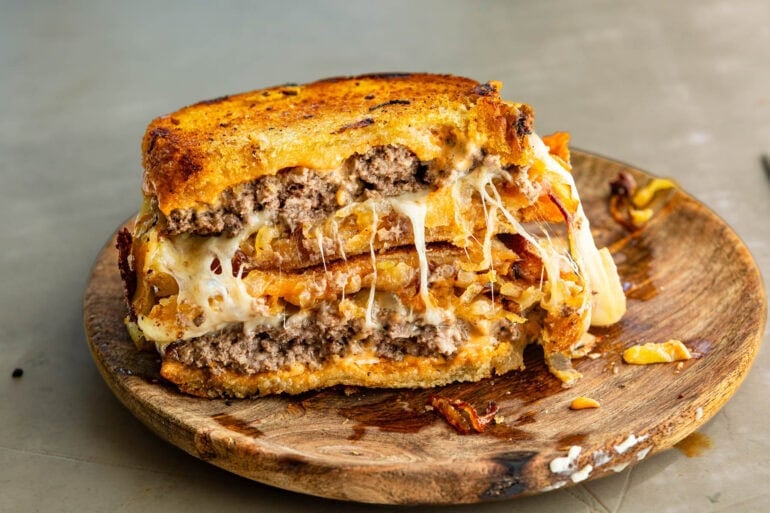 a patty melt broken in half and stacked on each other showing the inside of the patty melt sitting on a wooden cutting board