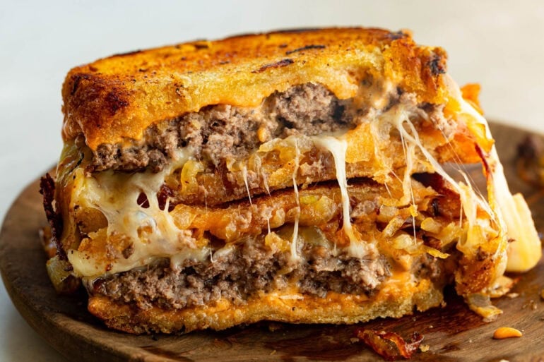 a patty melt that is broken in half and stacked on each other so you can see the inside of the patty melt with melty cheese and juicy patties