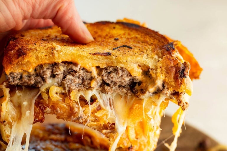 someone pulling apart two sides of a patty melt so you can see the melty, stringy cheese