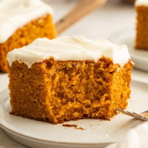 a piece of pumpkin cake topped with cream cheese frosting and a bite taken out of the corner