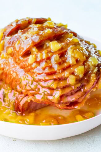 a photo of a spiral cut ham topped with a juicy pineapple glaze on a large white serving platter