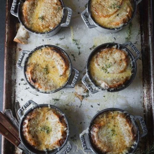 A baking sheet with containers of Onion soup. The soup has a bread and cheese topping that has been toasted in the oven.
